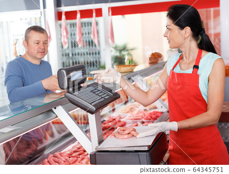 Female seller weighing sausages for customer 64345751