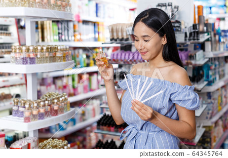 Girl with testers in perfumery, choosing perfume in cosmetic shop Girl with testers in perfumery, choosing perfume in cosmetic shop 64345764