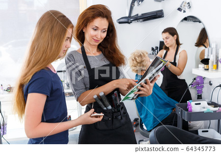 Hairdresser with teen girl looking at magazine Hairdresser with teen girl looking at magazine 64345773