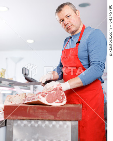 Portrait of man seller cutting meat in shop Portrait of man seller cutting meat in shop 64345790