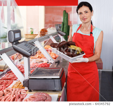 Female seller showing sausages in shop Female seller showing sausages in shop 64345792
