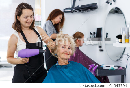 Hairdresser drying hair of elderly female Hairdresser drying hair of elderly female 64345794