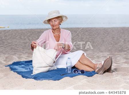 Elderly woman relaxing on beach 64345878