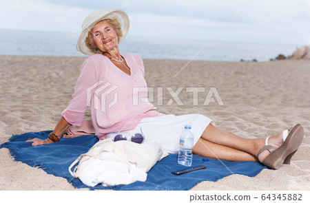 Elderly woman relaxing on beach 64345882