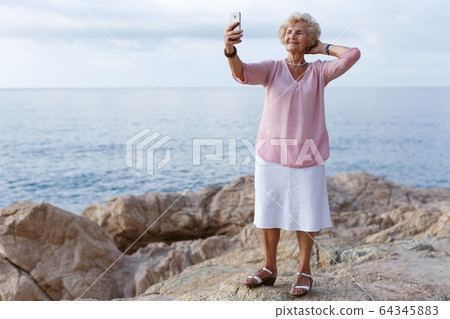 Mature woman taking selfie on beach Mature woman taking selfie on beach 64345883
