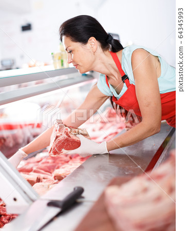 Adult woman seller displaying fresh meat in shop 64345993