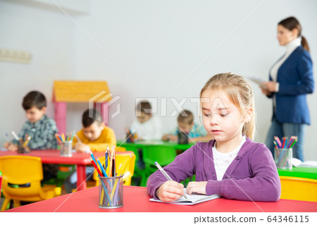 Portrait of little assiduous girl with pen and notebook at lesson in elementary school Portrait of little assiduous girl with pen and notebook at lesson in elementary school 64346115