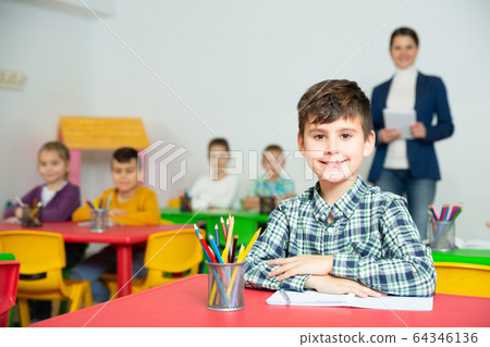 Portrait of little assiduous boy with pen and notebook at lesson in elementary school 64346136