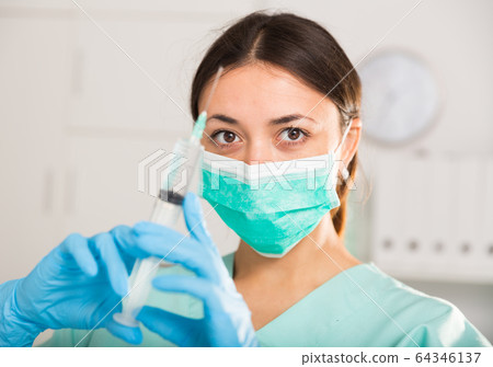 Female nurse in mask holding syringe for injection in hospital Female nurse in mask holding syringe for injection in hospital 64346137