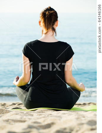 Adult female in black T-shirt is sitting her back and practicing asana Adult female in black T-shirt is sitting her back and practicing asana 64346166
