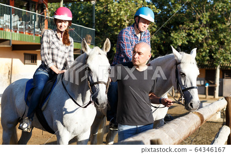Positive mature couple with jockey learn to riding horse at farm Positive mature couple with jockey learn to riding horse at farm 64346167
