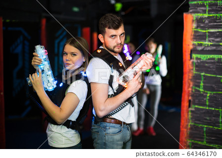 Couple standing back to back with laser guns 64346170