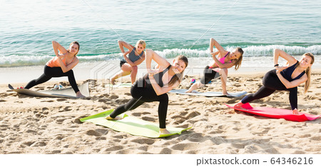 Slender women exercising yoga poses on sunny beach 64346216