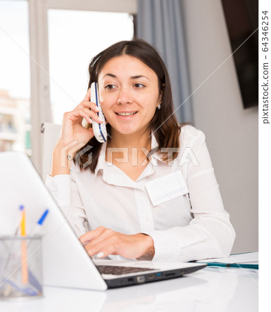 Young woman using laptop and talking by phone at the office Young woman using laptop and talking by phone at the office 64346254