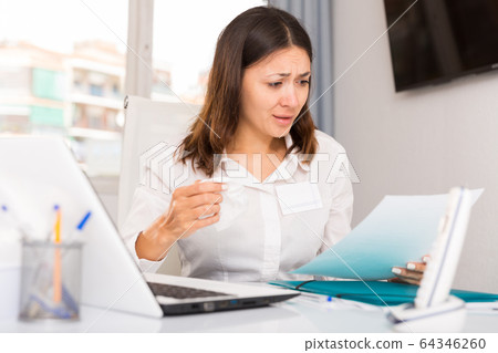 Upset woman reading documents and holding napkin at the office Upset woman reading documents and holding napkin at the office 64346260