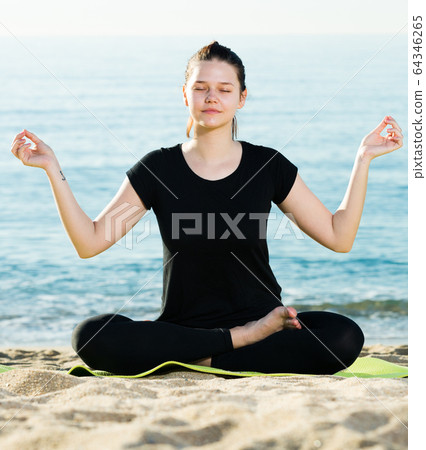 Sportswoman in black T-shirt is sitting and practicing yoga Sportswoman in black T-shirt is sitting and practicing yoga 64346265