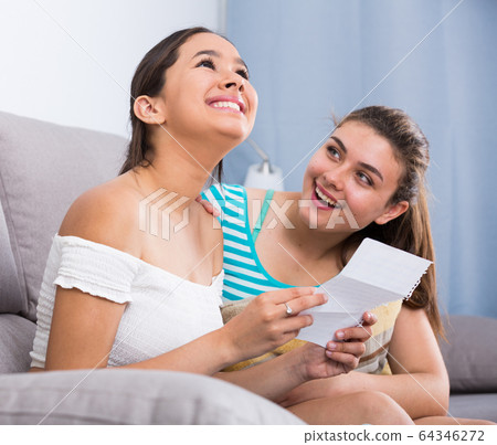 Teenagers girls reading letter on couch Teenagers girls reading letter on couch 64346272