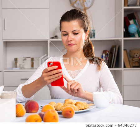Smiling woman with phone during breakfast 64346273