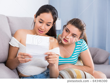 Teenagers girls reading letter on couch 64346300