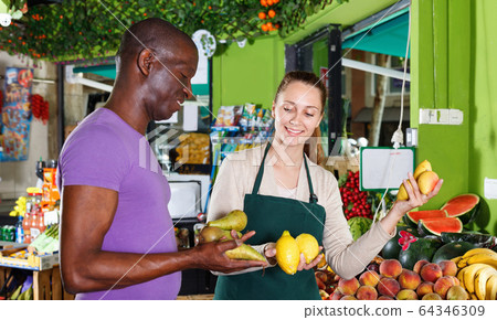 Seller woman is helping man choose fresh fruits in the market. Seller woman is helping man choose fresh fruits in the market. 64346309