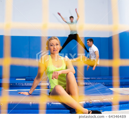Smiling woman taking break during workout on trampoline Smiling woman taking break during workout on trampoline 64346489