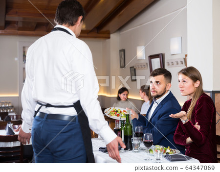 grumpy guests conflicting with waiter in restaurant 64347069