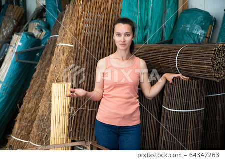 Female seller offers decorative fence of twigs in store Female seller offers decorative fence of twigs in store 64347263
