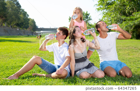 Family sitting on green lawn and drinking water Family sitting on green lawn and drinking water 64347265