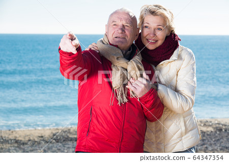Mature couple pointing on beach Mature couple pointing on beach 64347354
