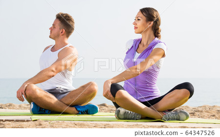 Cross-legged couple practice yoga on beach in morning 64347526