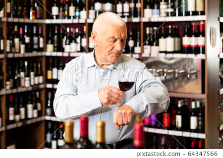 Elderly man checks the color and taste of red wine in a liquor store Elderly man checks the color and taste of red wine in a liquor store 64347566