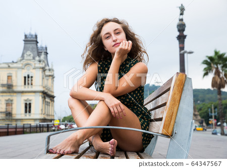 Attractive girl tourist sitting at wooden bench and thinking in center Attractive girl tourist sitting at wooden bench and thinking in center 64347567
