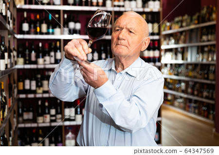Portrait of senior man tasting red wine at wine shop 64347569