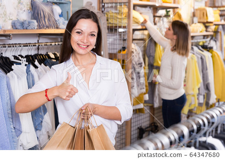 Young woman with paper bags holding thumb up in fashion store Young woman with paper bags holding thumb up in fashion store 64347680