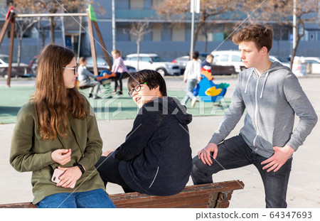 Three teenagers are talking about play on walk in the playground 64347693