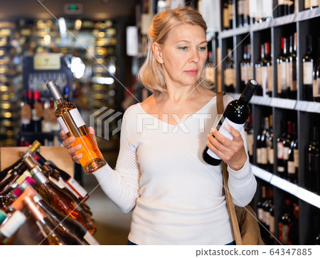Portrait of mature woman visiting winehouse in search of bottle of good wine 64347885