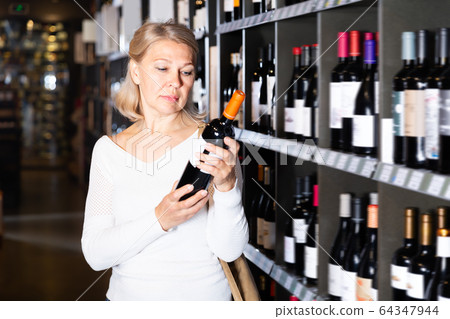 Attentive woman choosing bottled wine 64347944