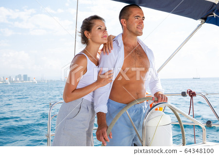 Woman and man steering yacht along shoreline of Spain Woman and man steering yacht along shoreline of Spain 64348100