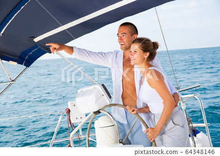 Man on yacht wheel pointing to horizon 64348146