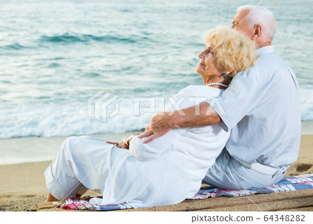 man and woman sitting on the sea shore 64348282