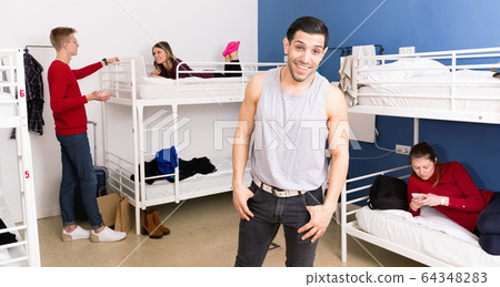 Handsome Hispanic man smiling while standing in bedroom of hostel 64348283