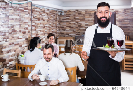 Smiling waiter taking care of adults at cafe table Smiling waiter taking care of adults at cafe table 64348644