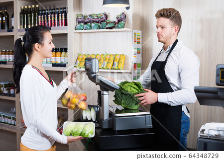 Seller assisting customer to weigh purchases Seller assisting customer to weigh purchases 64348729