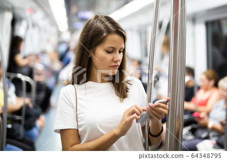 Woman holding smartphone in subway car Woman holding smartphone in subway car 64348795