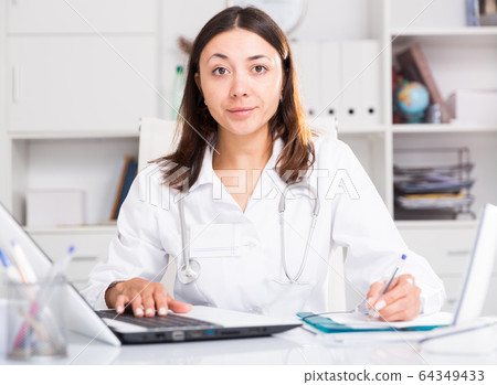 Practicioner girl in medical uniform is working with documents and laptop 64349433