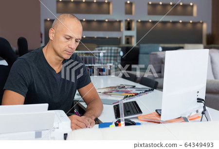 Portrait of male shop assistant in process of working with pc in furniture salon 64349493
