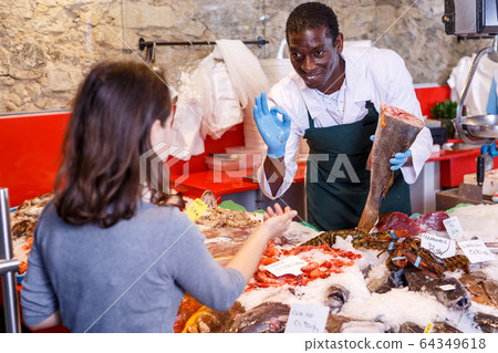 Salesman serving customer raw fish 64349618