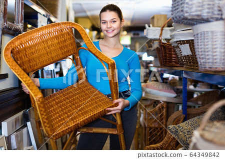 Young customer woman standing with wicker chair in shop for decor Young customer woman standing with wicker chair in shop for decor 64349842