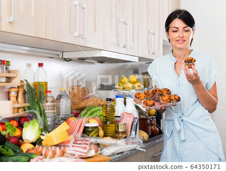 Female is posing with cupcakes in time cooking on the kitchen at home. Female is posing with cupcakes in time cooking on the kitchen at home. 64350171