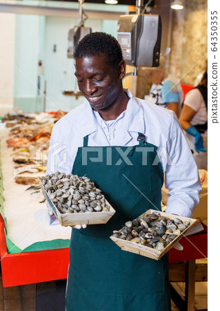 Salesman offering fresh clams in fish store 64350355